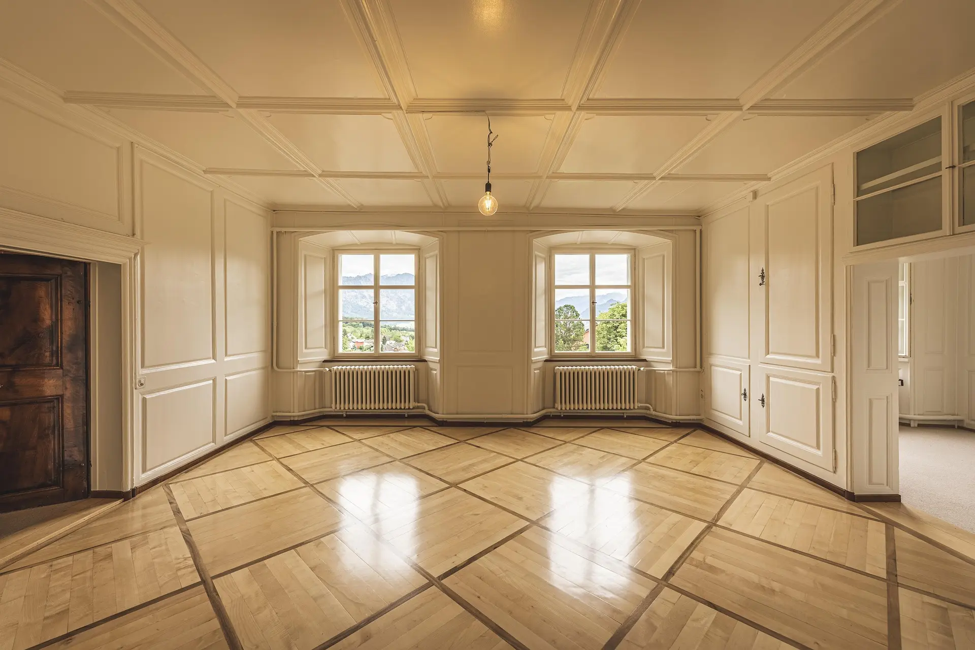 Ampio salone con parquet, soffitto decorato, due finestre e apertura verso una stanza adiacente